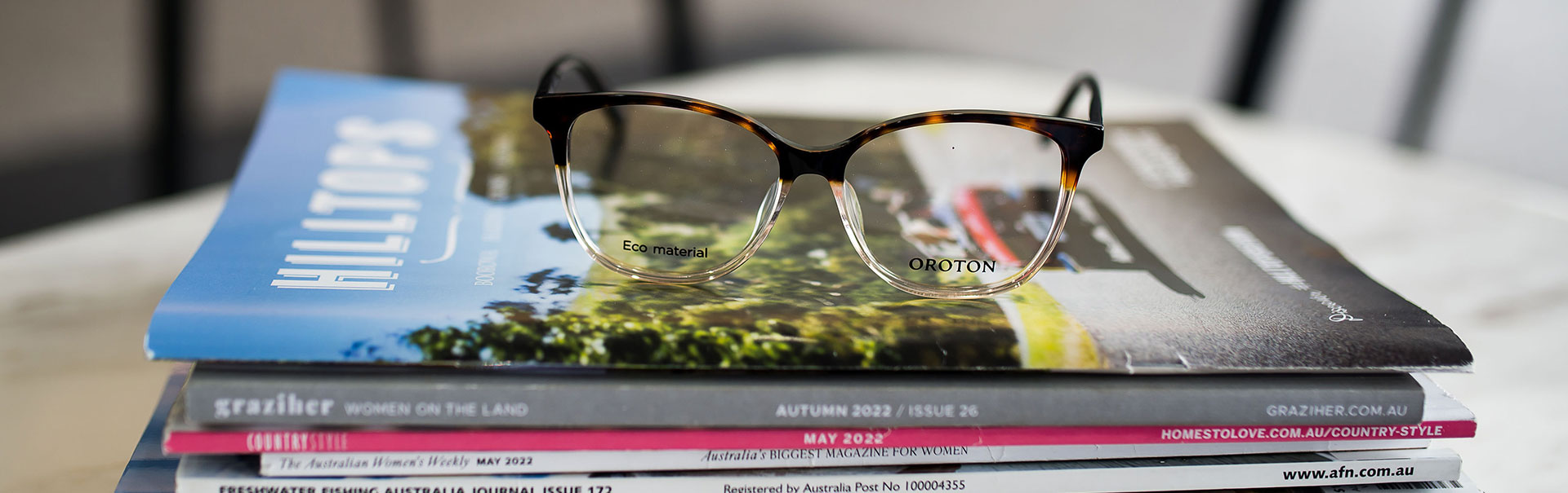 A pair of brown Oroton glasses on a stack of magazines