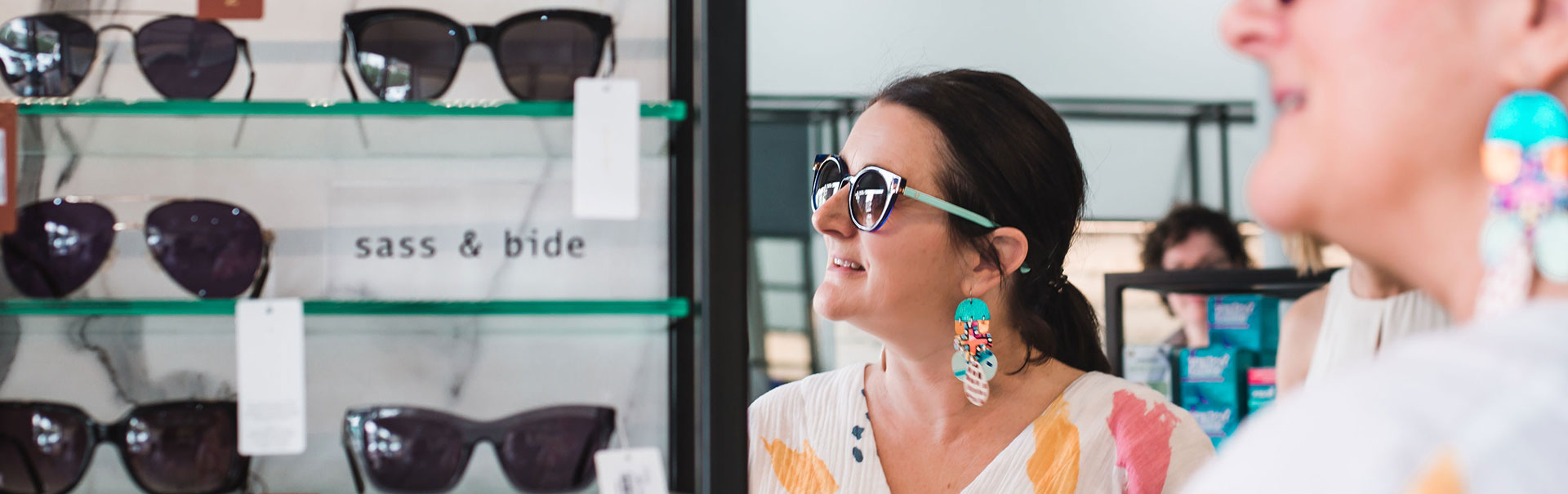 Brunette woman with colourful earrings trying on a pair of sunglasses